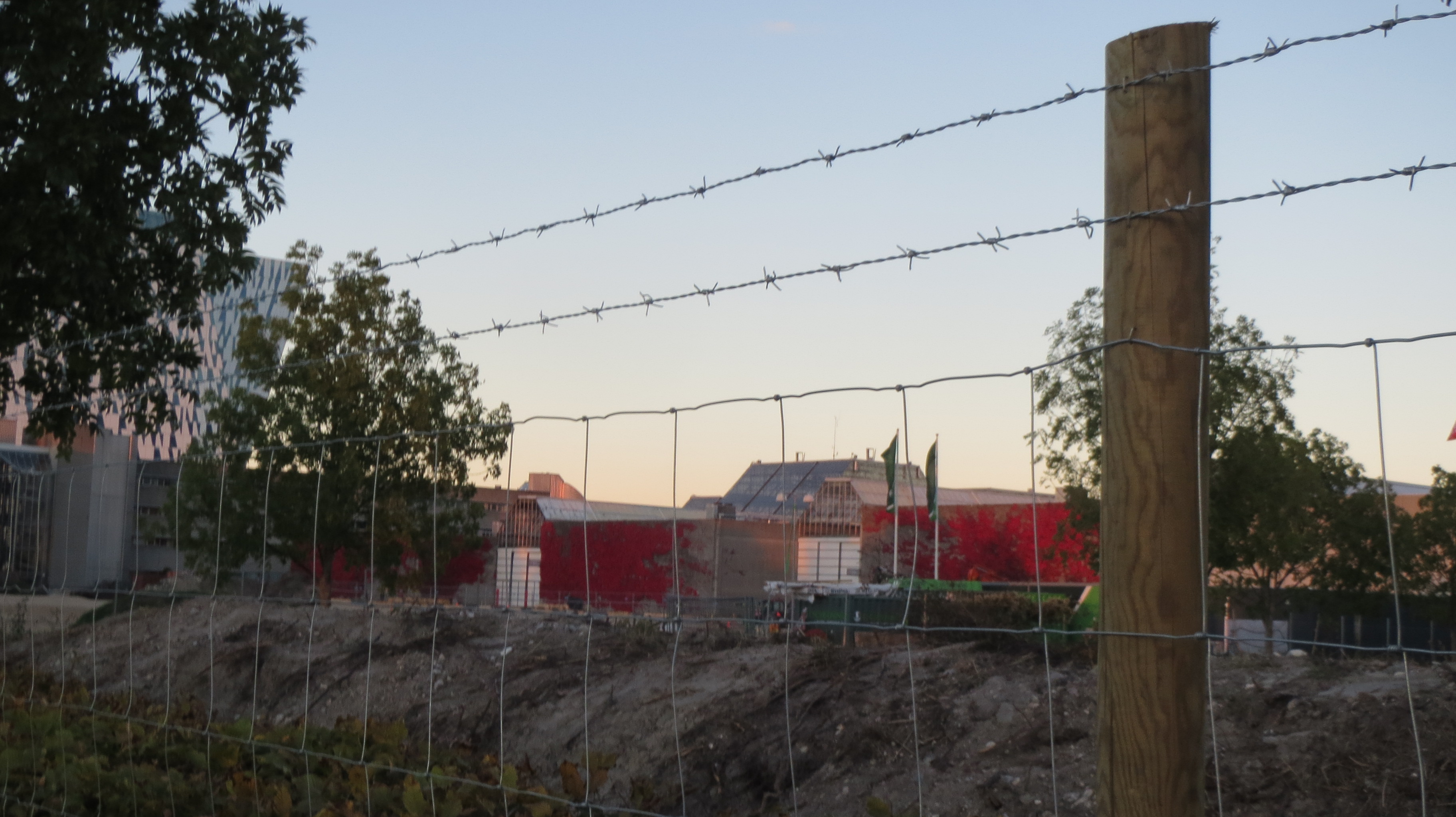 I bakgrunnen er en rød bygning, i forgrunnen er det et byggeplassgjerde