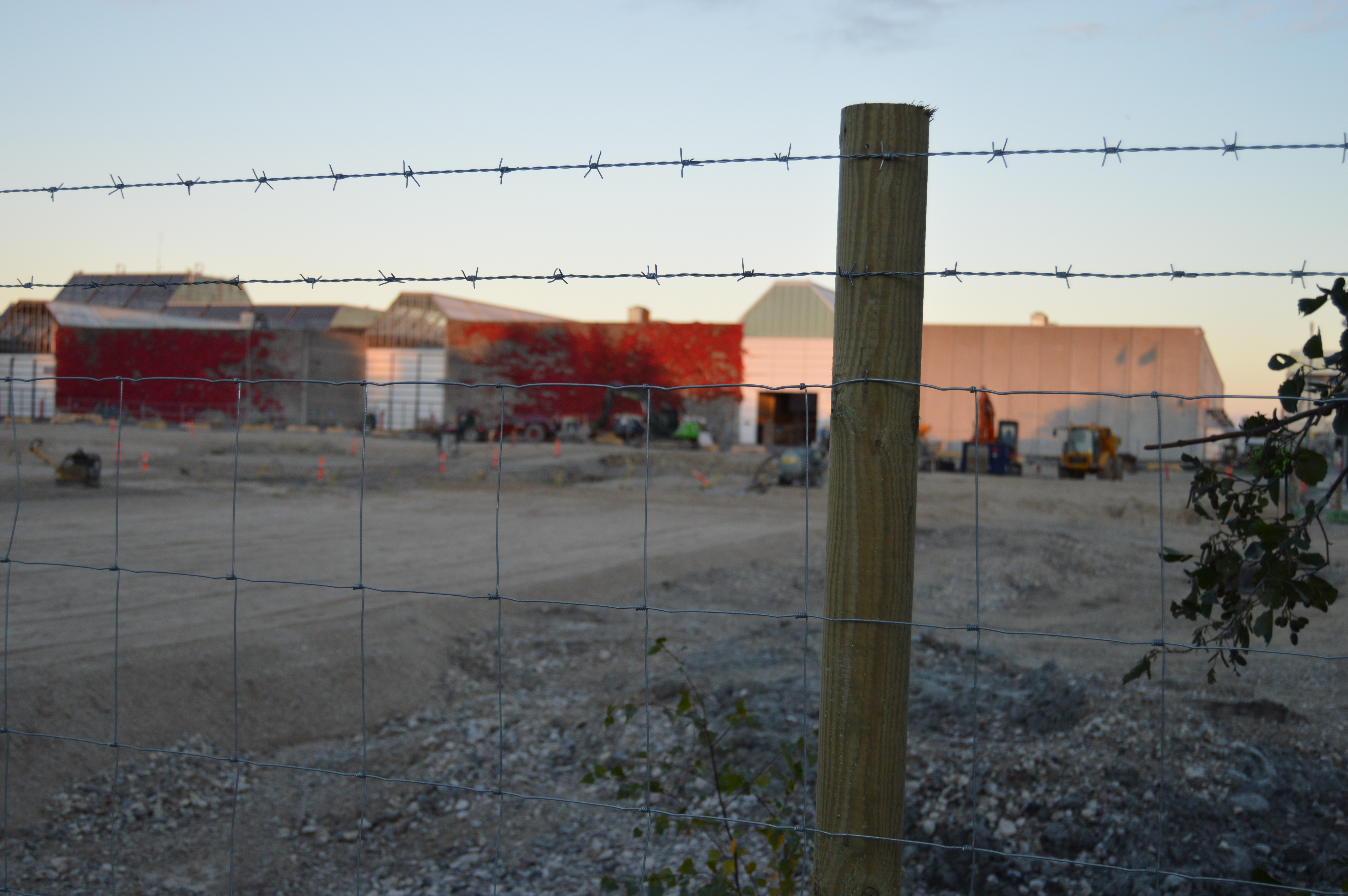 Et byggeplassgjerde og to rader med piggtråd er montert på en gjerdestolpe