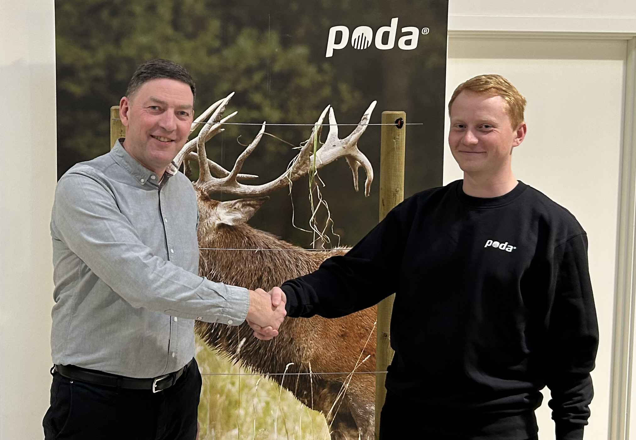 Poda-direktør Peter håndhilser på Sofus fra det nye Poda-senteret, Poda Hegn Ringe, foran et banner med hjort og elektrisk gjerde.