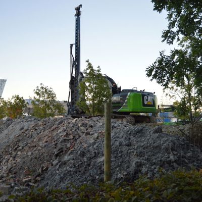 En grønn CAT-maskin står parkert på toppen av en grushaug. Maskinen er sikret med et byggeplassgjerde.