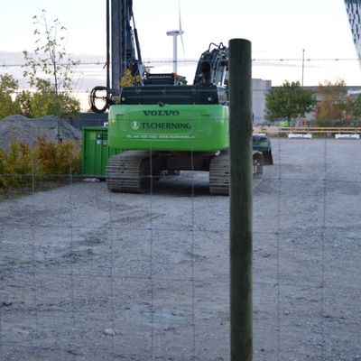 I forgrunnen er det et gjerde til en byggeplass. Bak gjerdet står en maskin