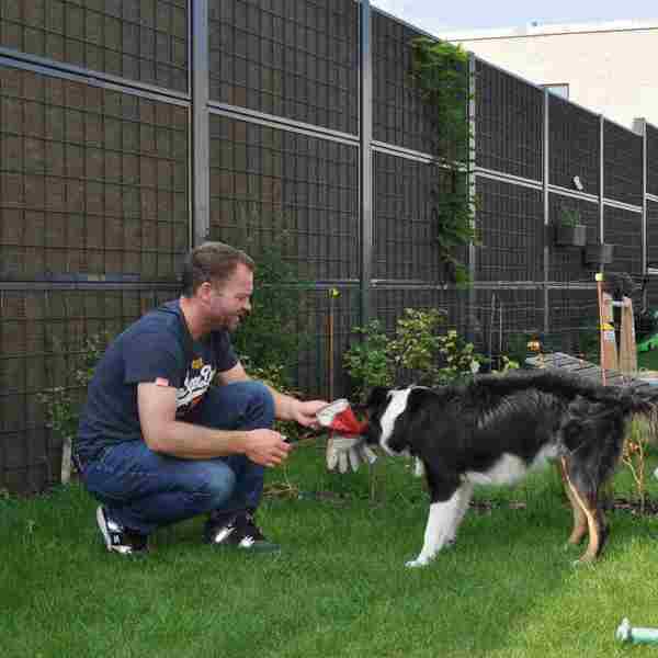 En mann og hunden hans sitter foran et Noistop® Steel-støygjerde fra Poda Gjerder som er installert i en hage for å skjerme for støy fra naboene