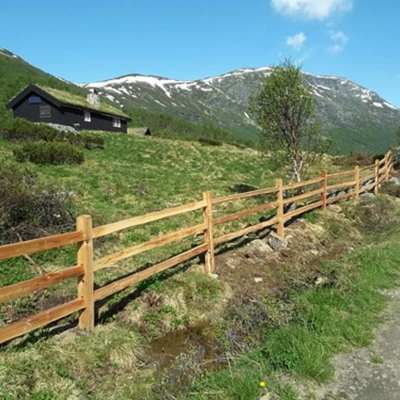 Et rustikt gjerde i sedertre avgrenser en naturtomt med hytte i et fjellområde.