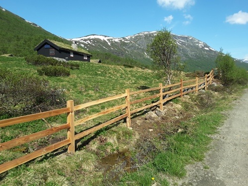 Et rustikt gjerde i sedertre avgrenser en naturtomt med hytte i et fjellområde.