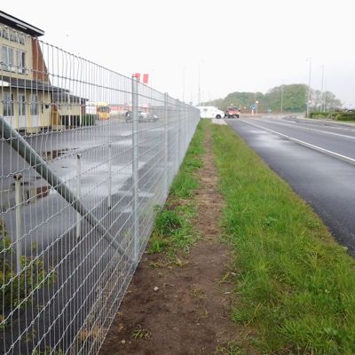 Et høyt Multinet-gjerde har blitt satt opp ved siden av en vei for å beskytte en bedrift