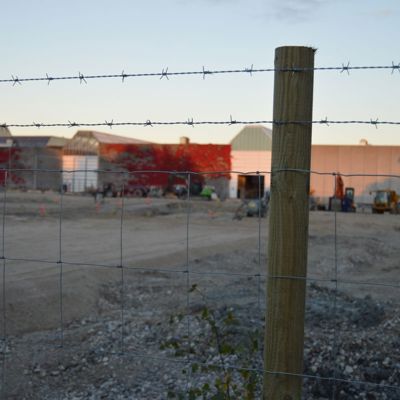 Et byggeplassgjerde og to rader med piggtråd er montert på en gjerdestolpe