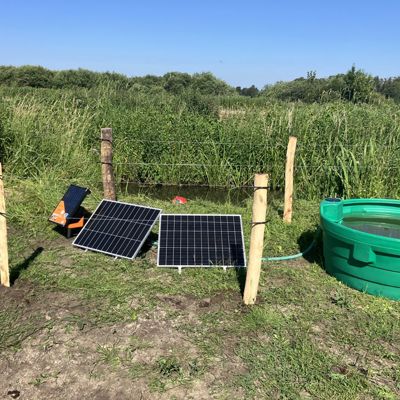 Soldrevet feltpumpe med solcellepaneler og drikkekar ved et inngjerdet bekk