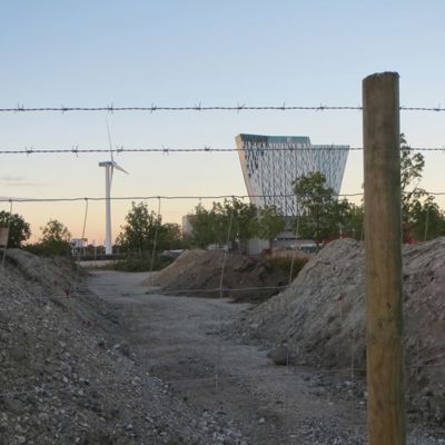 Et byggeplassgjerde bestående av trykkimpregnerte stolper, nettinggjerde og to rader med piggtråd