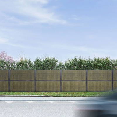 Noistop Essential støygjerde med antrasittgrå ramme, omgitt av grønn beplantning, med en fotgjenger og en forbipasserende bil i forgrunnen.